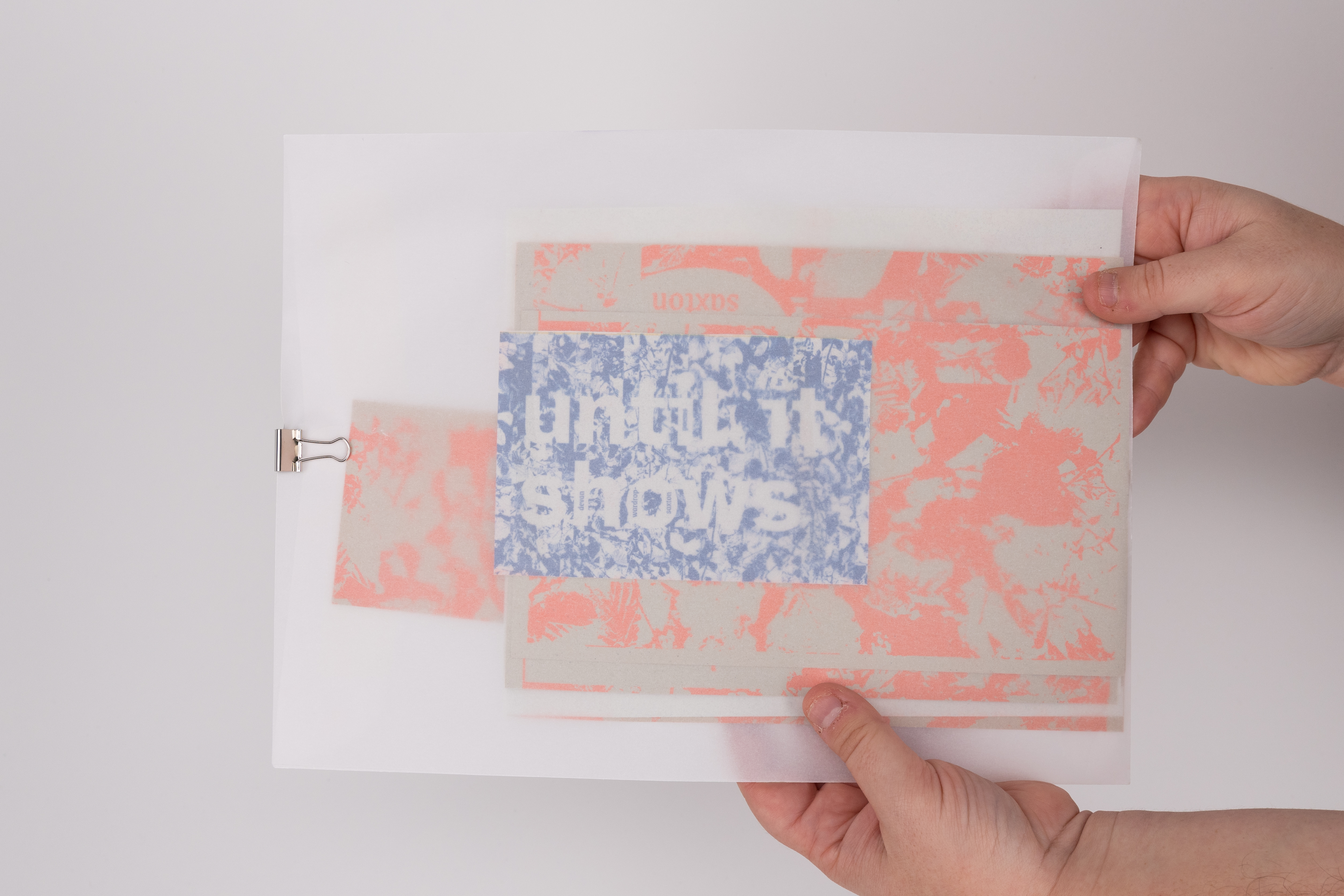 translucent envelope against a white background, the dark blue title card and bright orange, abstract riso prints showing through the envelope's surface